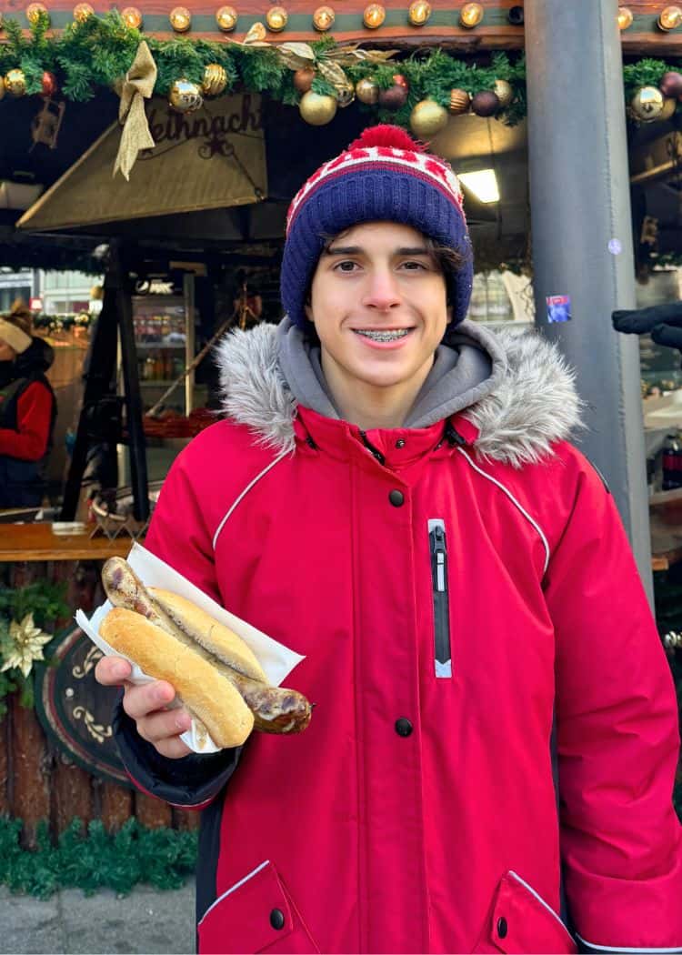 Christmas Market Foods - Boy in red coat holding a sausage on a bun